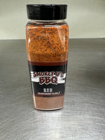 A plastic shaker bottle of Smokey D's BBQ rub seasoning - Championship Blend - with a black label and brown speckled contents visible through the bottle.