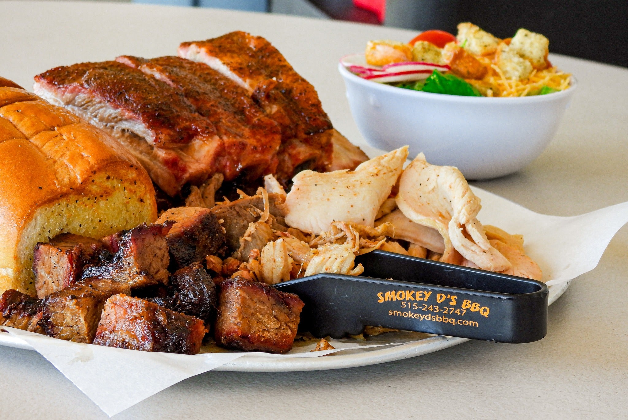 Platter of barbecue meats with a bowl of coleslaw and a bun, featuring Smokey D's BBQ branding.