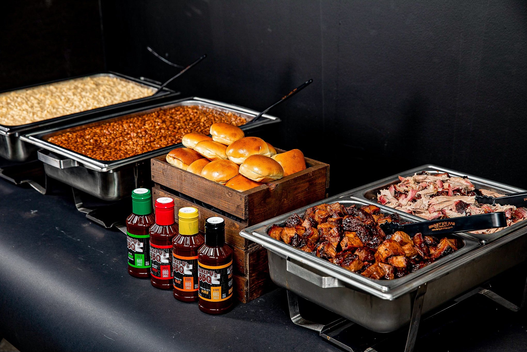Catering spread from Smokey D's BBQ featuring meats, sides, sauces, and rolls