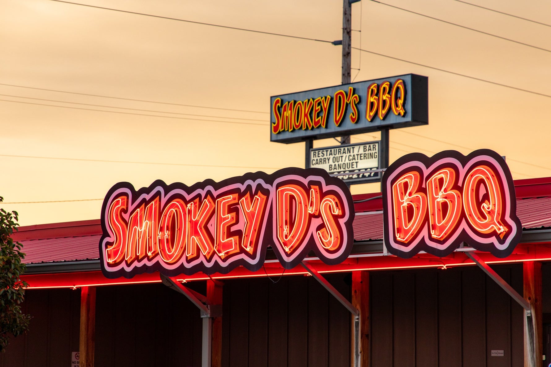 Neon sign for Smokey D's BBQ restaurant with a warm glow against a building.