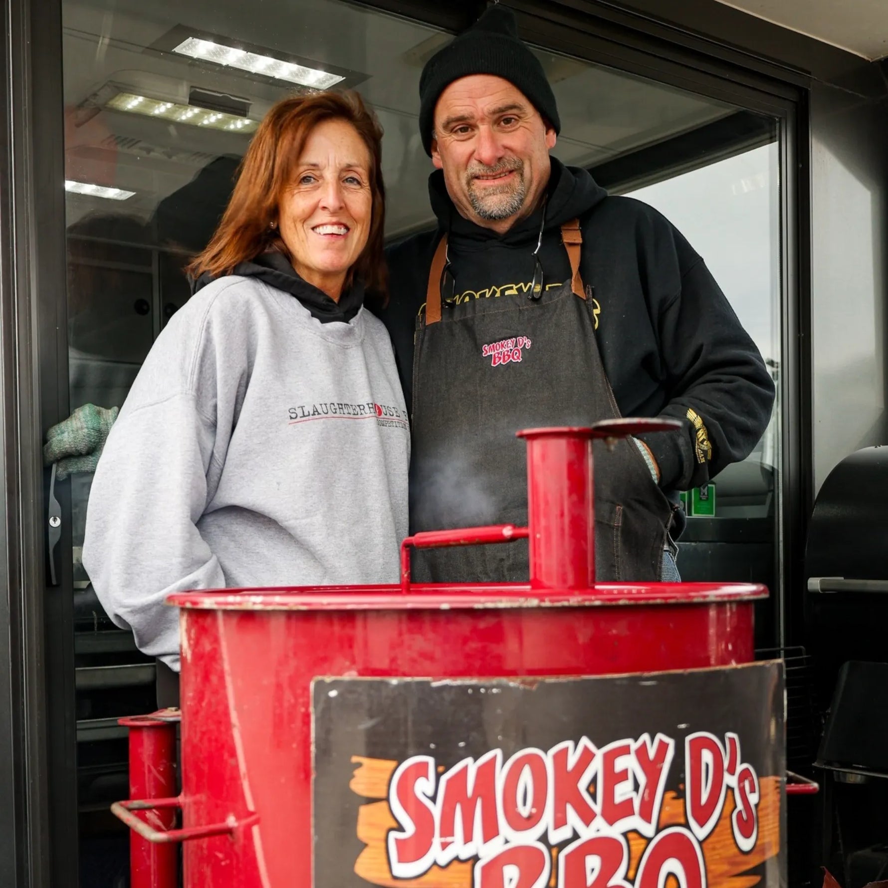 Darren and Sherry standing in front of Smokey D's BBQ sign