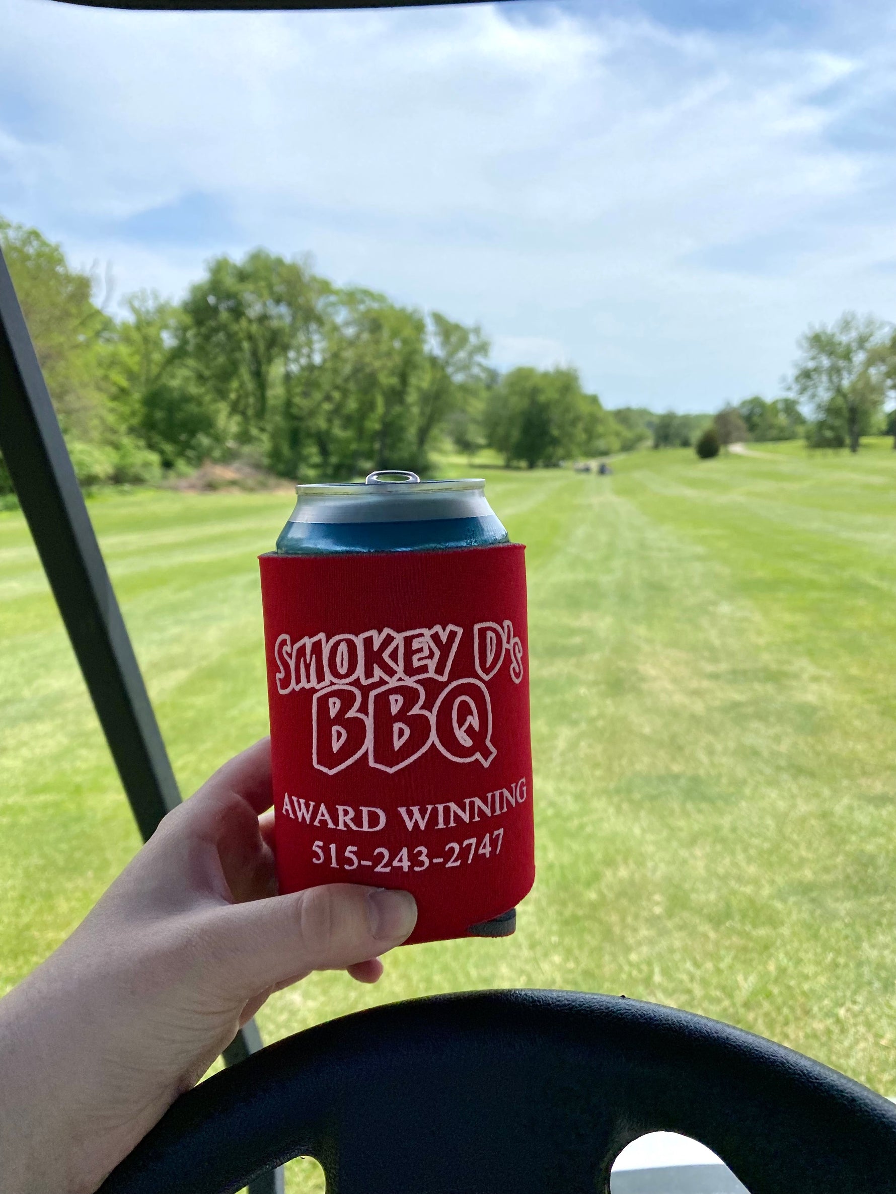 Person holding a soda in a red koozie with white text reading, "Smokey D's BBQ - Award Wining 515-243-2747"