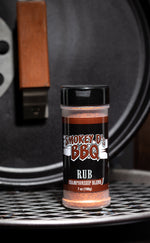 A 7 oz container of Championship Blend BBQ rub with a label that reads 'Smokey's BBQ RUB'. The container is placed on a grill.